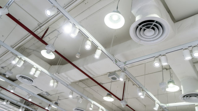 Bare ceiling with air duct, CCTV, air conditioner pipe and fire sprinkler system on white ceiling wall. Air flow and ventilation system. Ceiling lamp light with opened light. Interior architecture.
